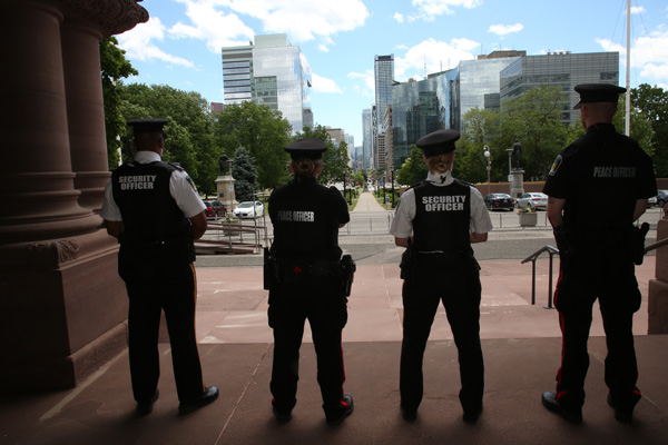 four officers with their backs to the camera facing out from the main entrance of the Legislative Building towards the front lawn