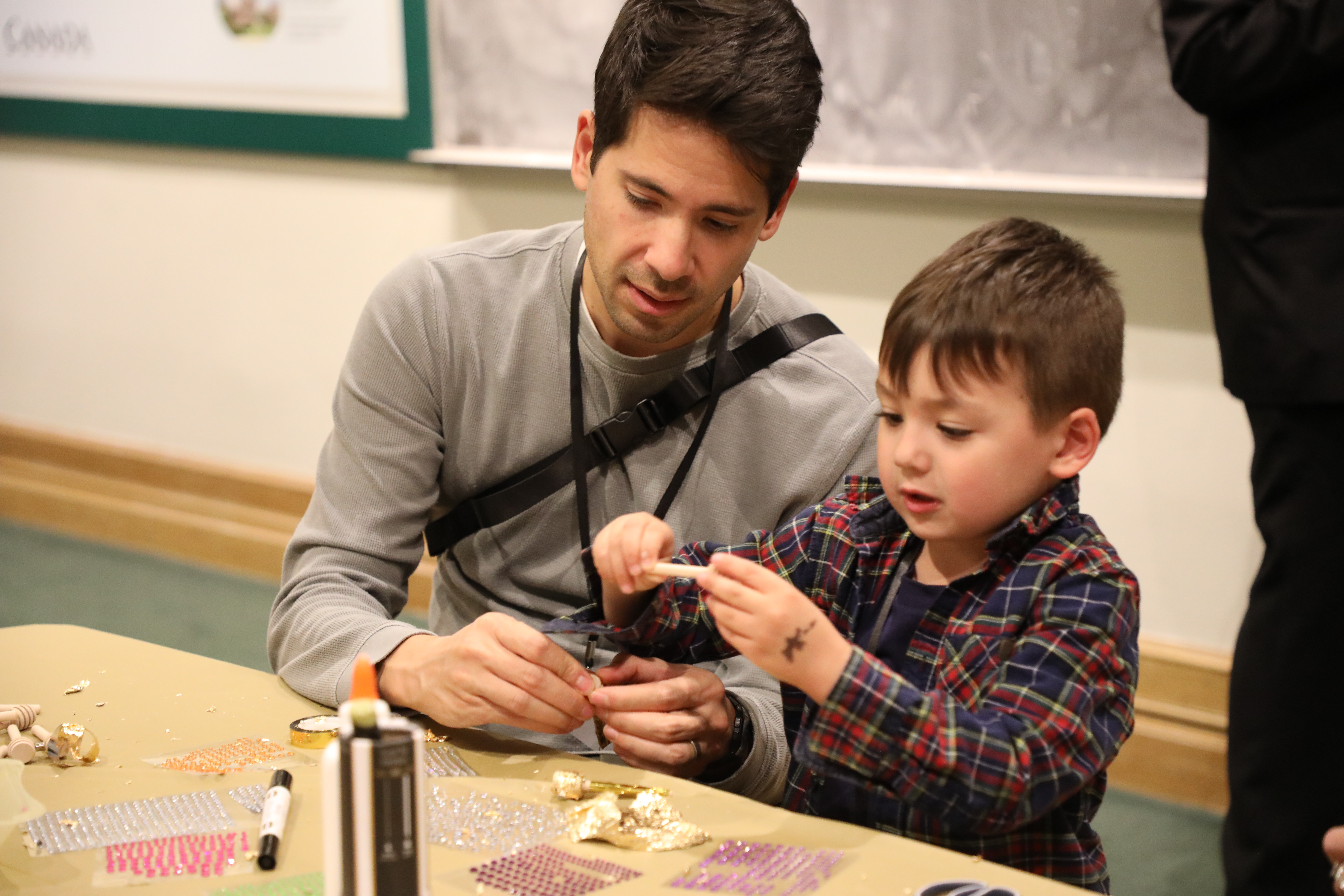 Un adulte et un enfant sont assis à une table et travaillent ensemble sur un projet artisanal avec des matériaux colorés.