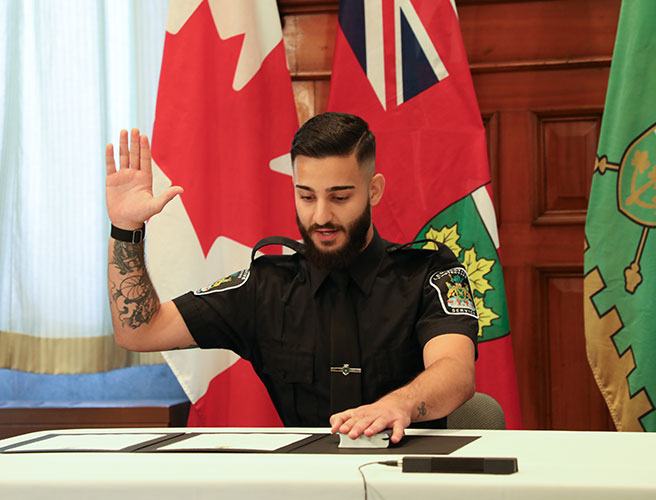 Officier du LPS assis au bureau, une main sur le livre et l'autre main levée